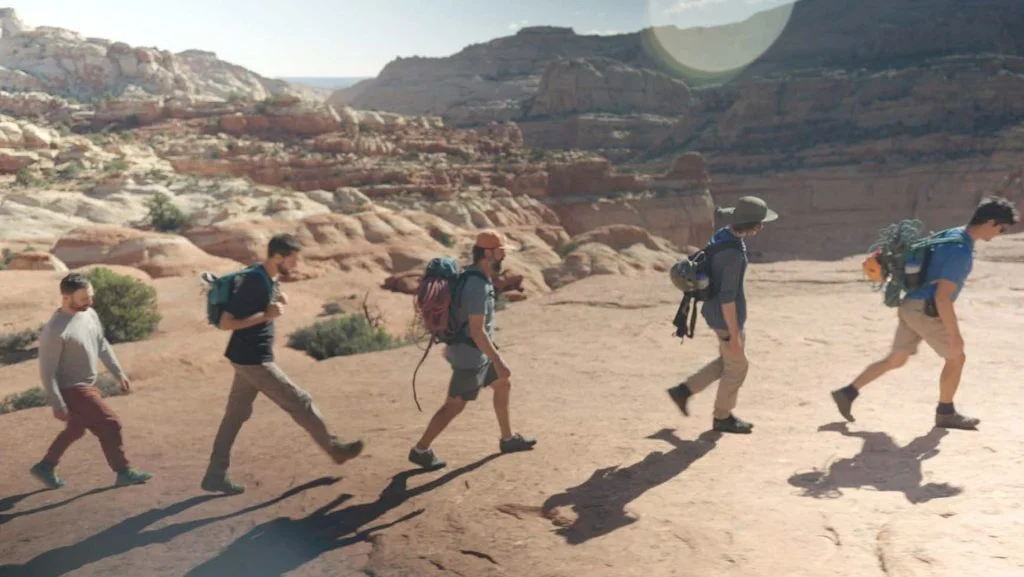 A group of men on a wilderness therapy expedition hike together through a desert canyon, symbolizing the forward momentum and peer support found on the journey to addiction and mental health recovery.