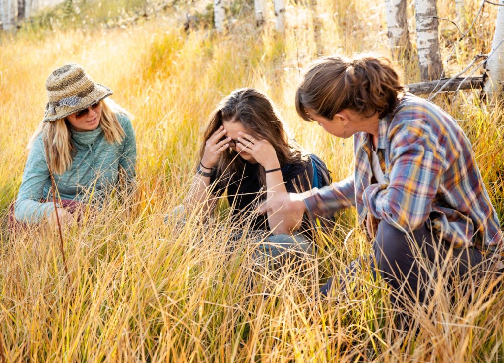 A young woman receives compassionate emotional support from her peers in a sunny field, showing how shared understanding helps in processing mental health challenges and anxiety.