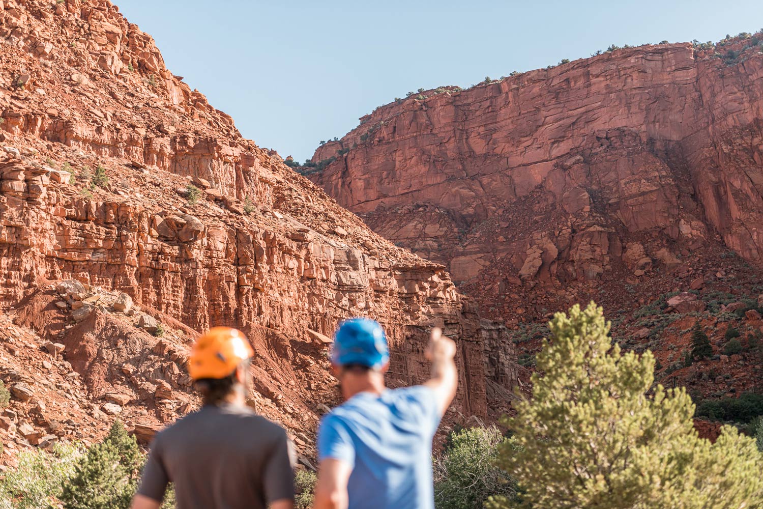 A mentor points out a route on a large rock wall to a young man, an exercise in goal-setting and overcoming perceived limitations as part of an adventure therapy program for men's mental health.