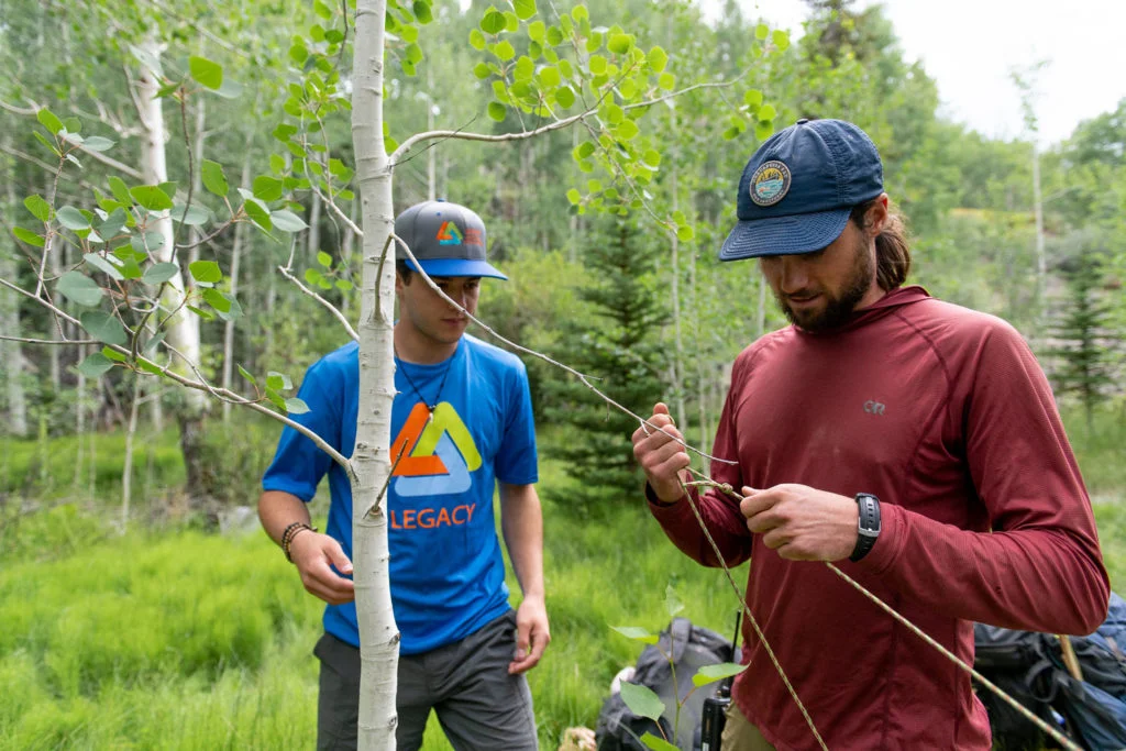 A mentor provides trauma-informed care by teaching a young man a practical skill in an aspen grove, an adventure therapy exercise designed to build focus, competence, and trust for mental health recovery.