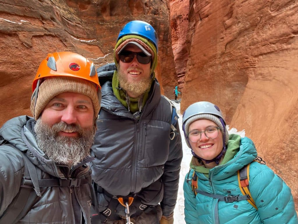 A therapist and two young adult clients smile together during a challenging canyoneering expedition, showcasing the positive relationships and resilience built through adventure therapy.